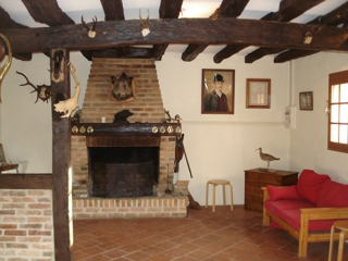 Vue de l'intérieur de la salle de chasse, centrée sur la cheminée dans le style traditionnel en brique et en bois.